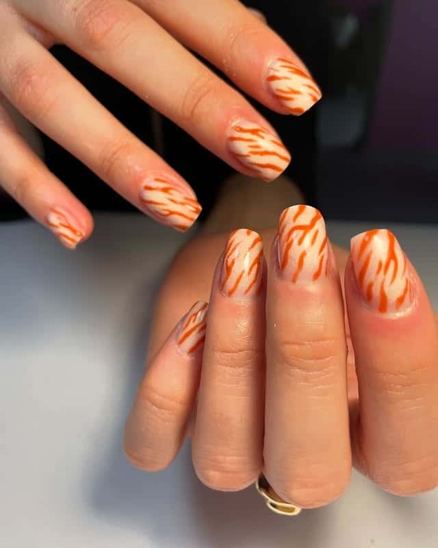 7. Orange Tiger Lines on Nudes - animal nail ideas