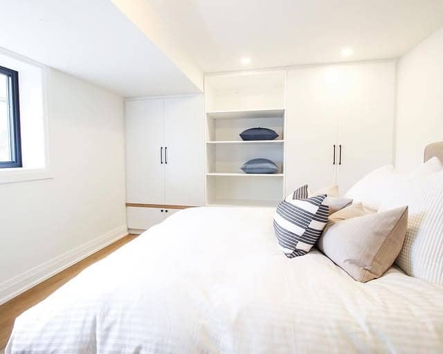 6. Streamlined Storage Wall with Fresh White Bedding - basement bedroom ideas
