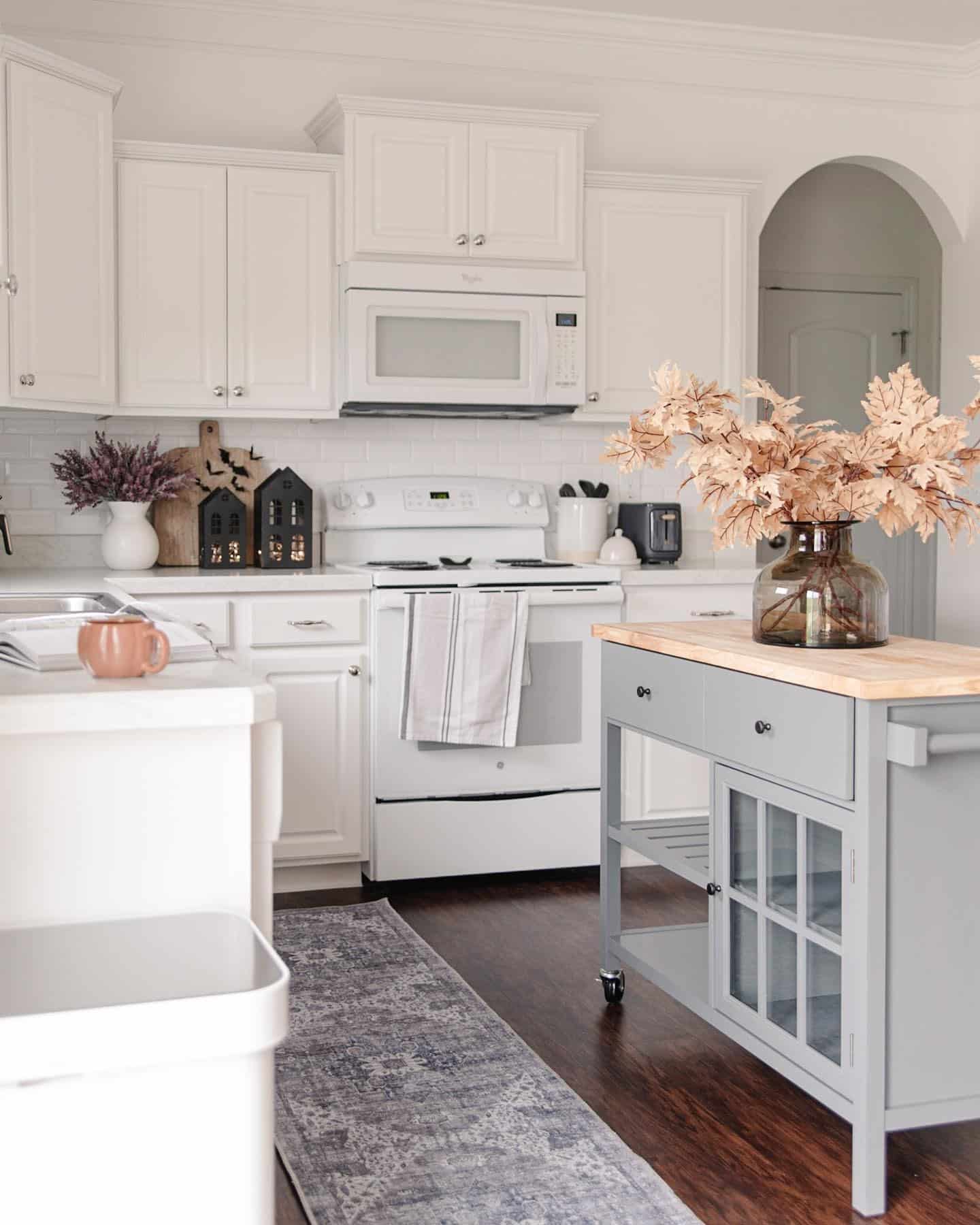 15. Classic White Kitchen with Blush Leaf Arrangement and Soft Gray Island - fall kitchen decor ideas