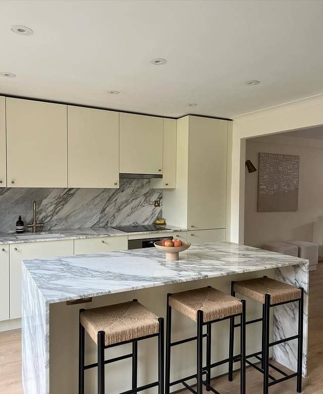 7. Cream Kitchen With Marble Waterfall Countertop and Minimal Cabinets - cream kitchen ideas