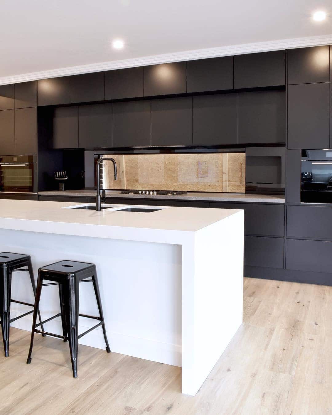 21. Minimal Black Cabinet Kitchen with White Waterfall Island - white and black kitchen ideas