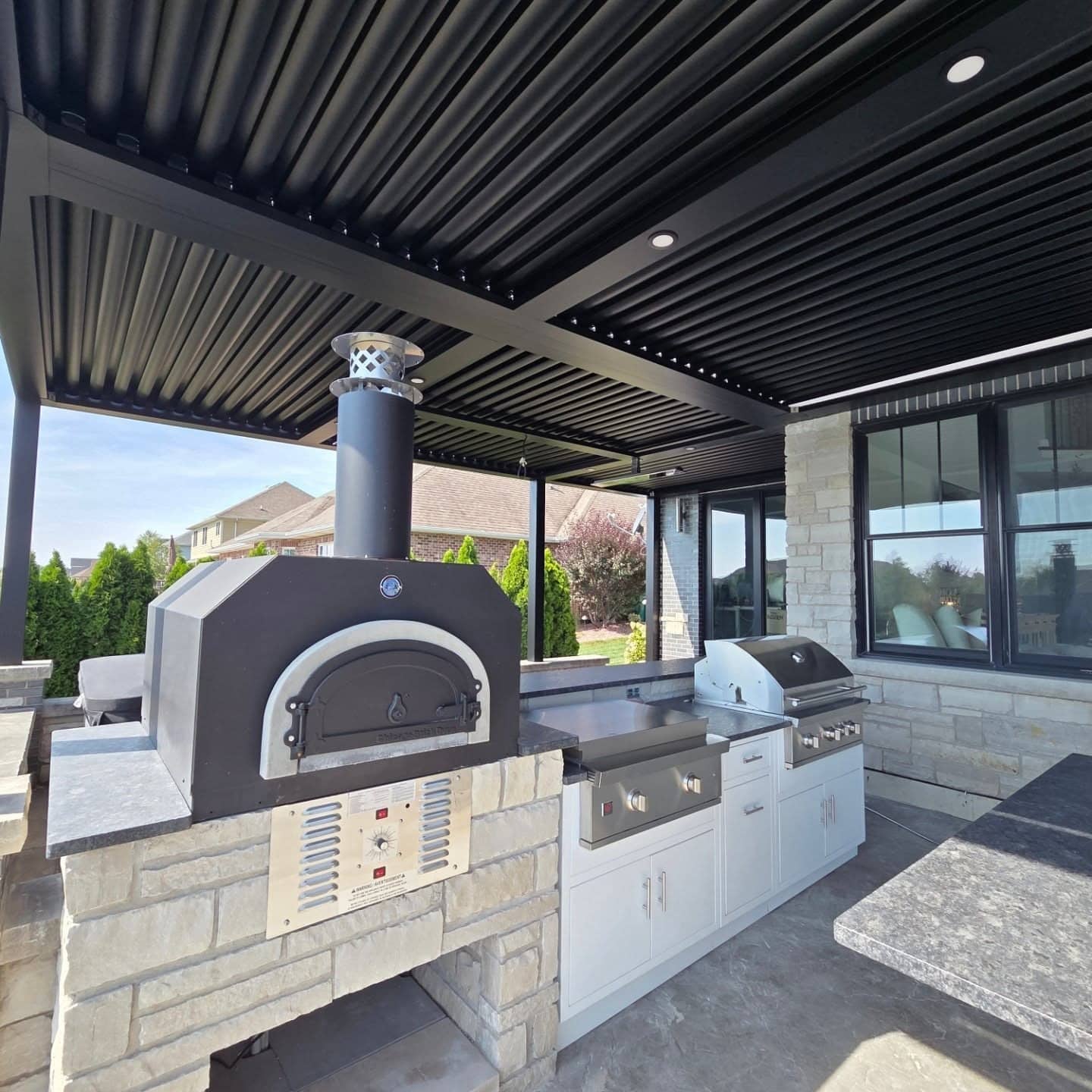 11. Contemporary Outdoor Kitchen with Black Pergola and Light Stone Accents - outdoor kitchen ideas