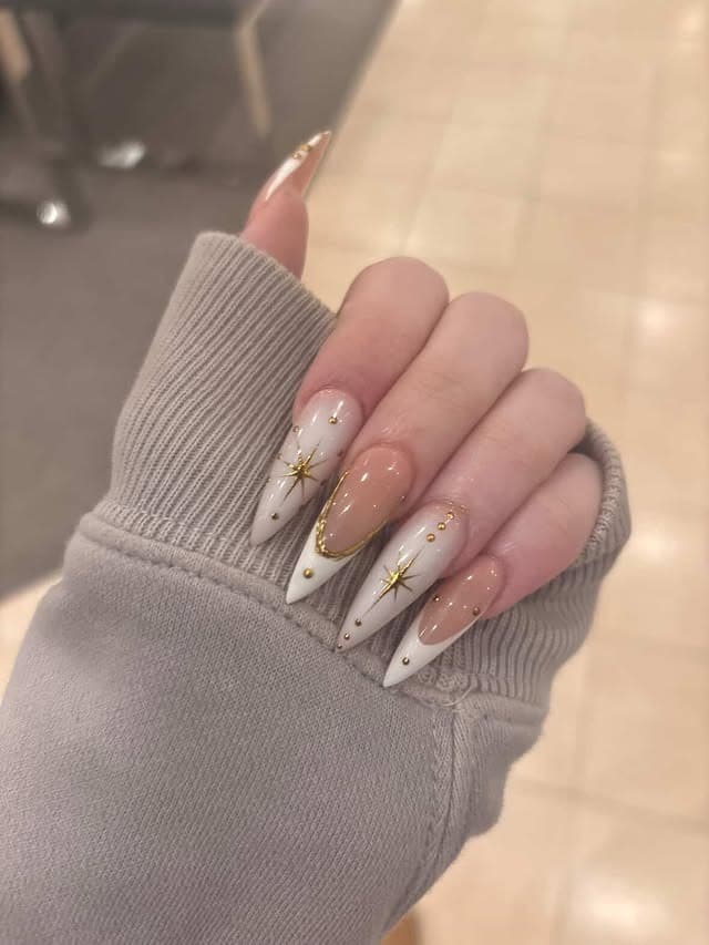 21. Milky White Stiletto Nails with Gold Starburst Accents - bling nail ideas